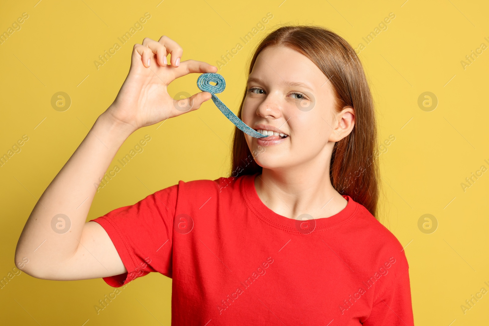 Photo of Teenage girl eating tasty gummy candy on yellow background