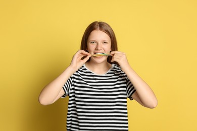 Teenage girl eating tasty rainbow sour belt on yellow background