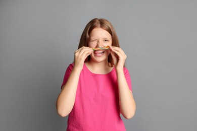 Happy teenage girl with tasty rainbow sour belt on grey background