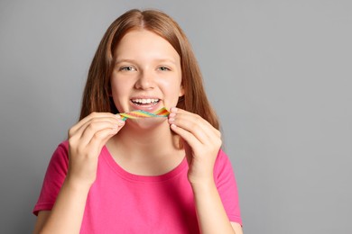 Photo of Happy teenage girl with tasty rainbow sour belt on grey background