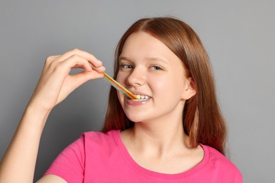 Photo of Teenage girl eating tasty rainbow sour belt on grey background