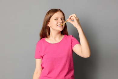 Teenage girl eating tasty rainbow sour belt on grey background