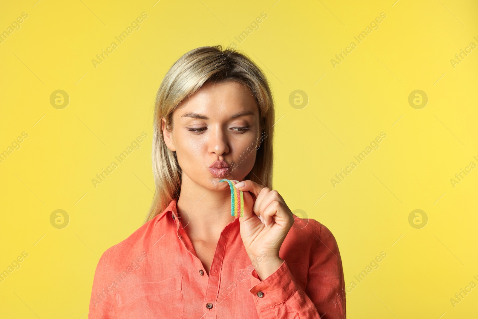 Photo of Young woman eating tasty rainbow sour belt on yellow background