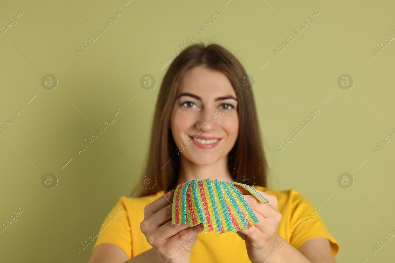 Photo of Happy young woman with tasty rainbow sour belts on olive background, selective focus