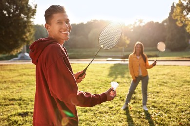 Photo of Young man and woman playing badminton in park on sunny day, selective focus