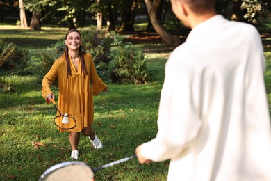 Young woman and man playing badminton in park, selective focus