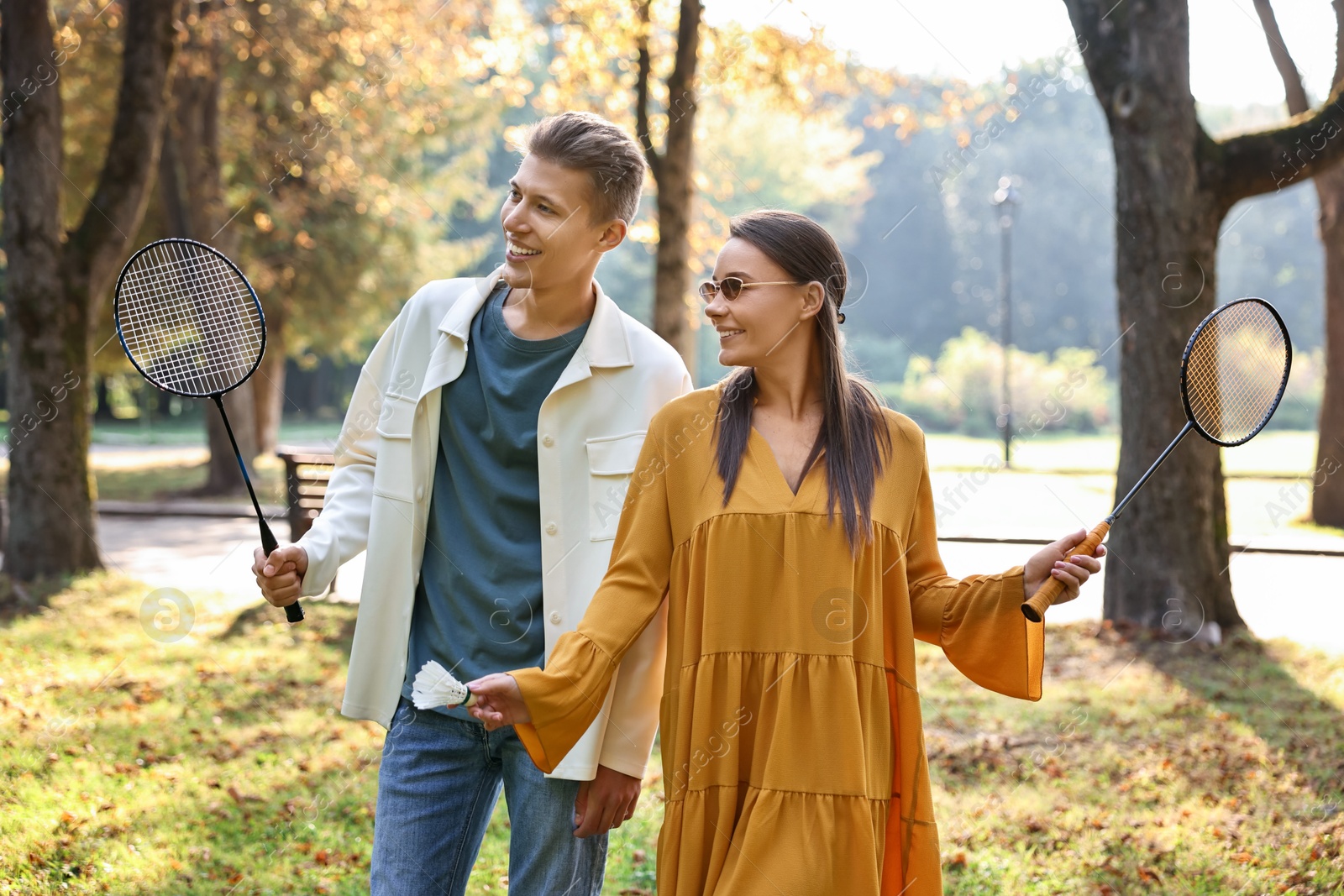 Photo of Young man and woman with badminton rackets and shuttlecock in park on sunny day