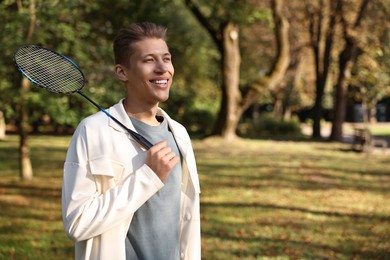 Happy young man with badminton racket in park, space for text