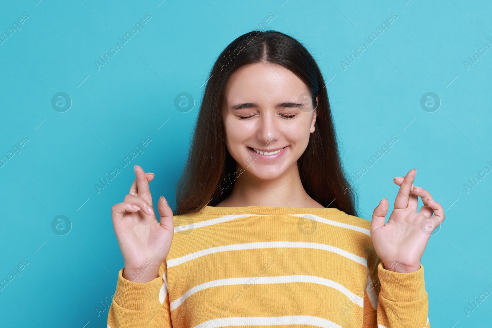 Photo of Excited young student crossing fingers on light blue background. Hope for good exam result