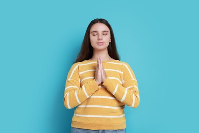 Photo of Young student praying for good exam result on light blue background