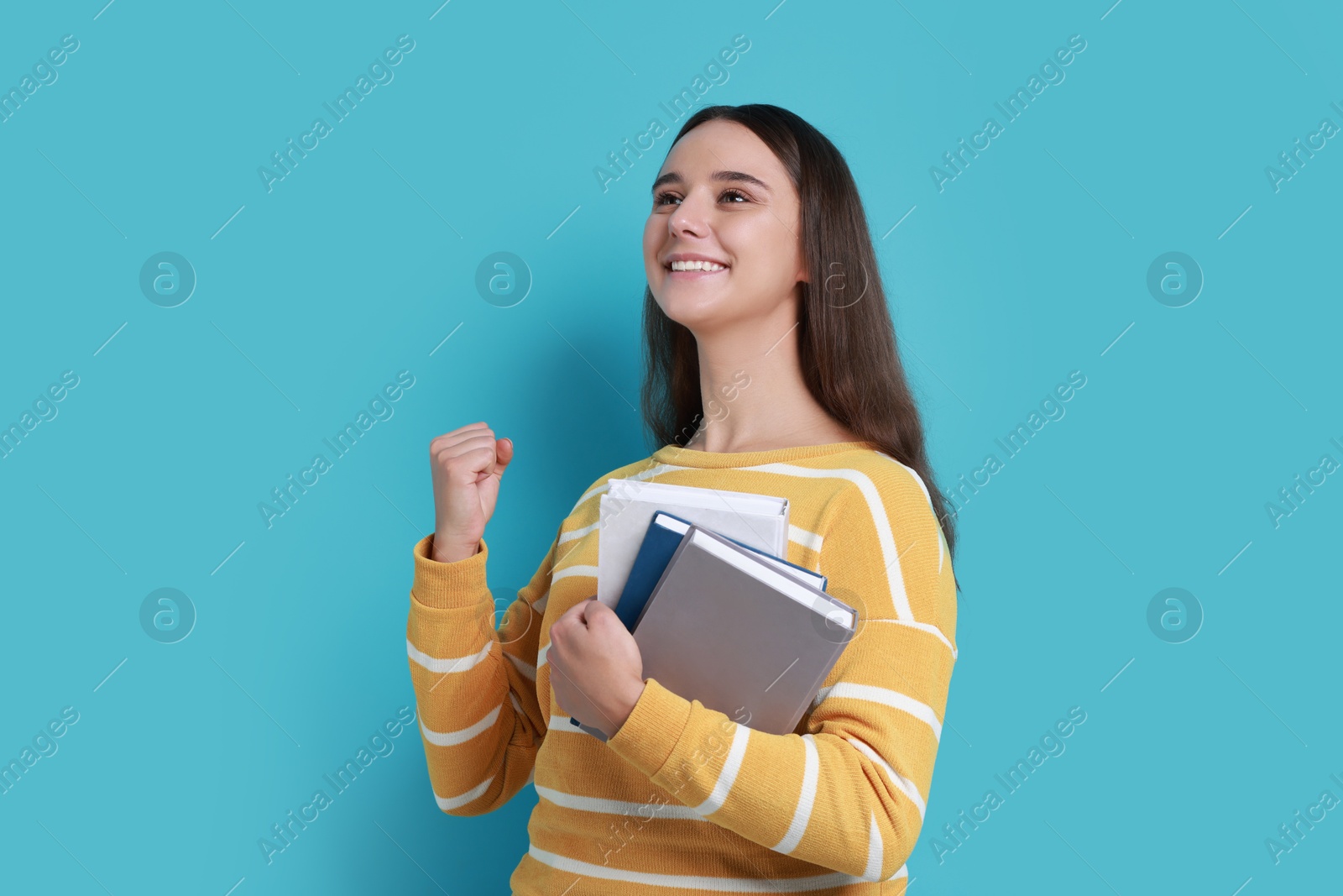 Photo of Young student with books happy about her good exam result on light blue background