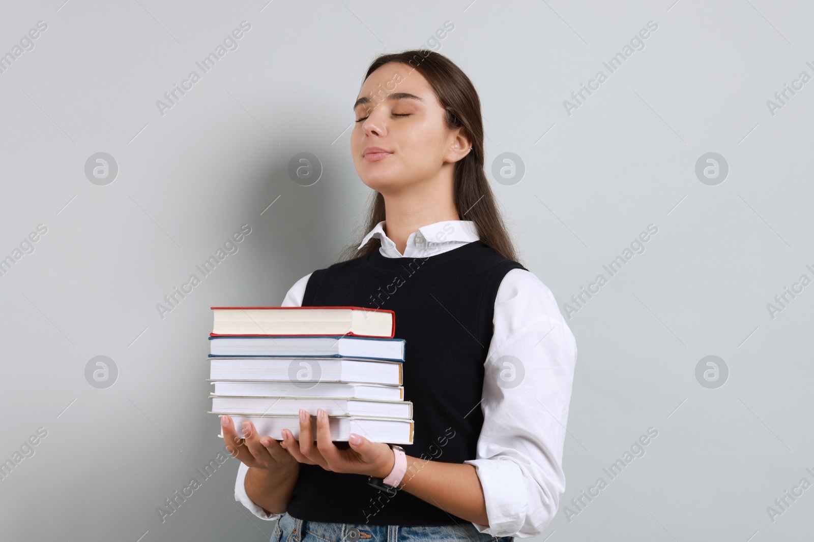 Photo of Young student with stack of books on grey background