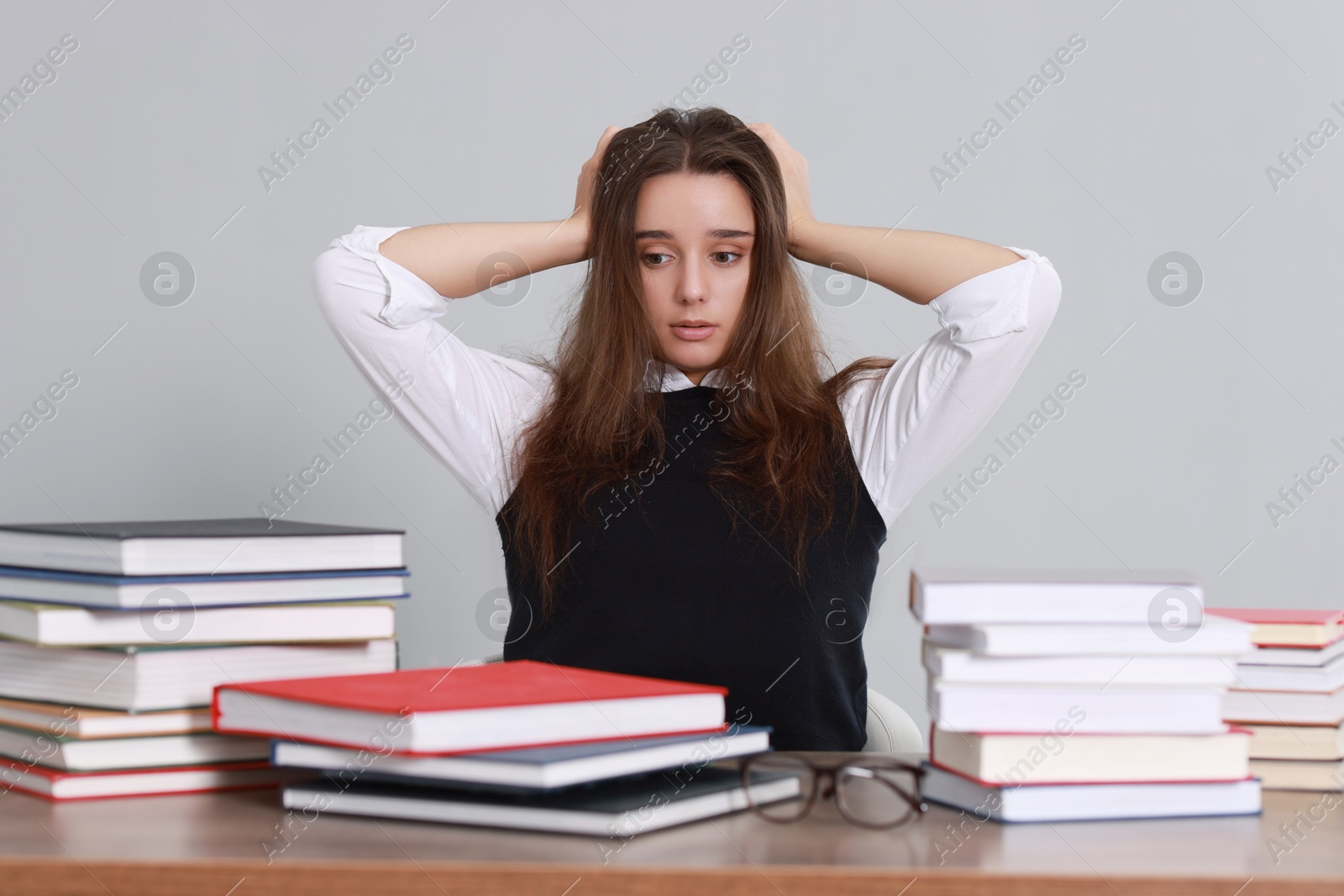 Photo of Young student having stress before exam at desk against grey background