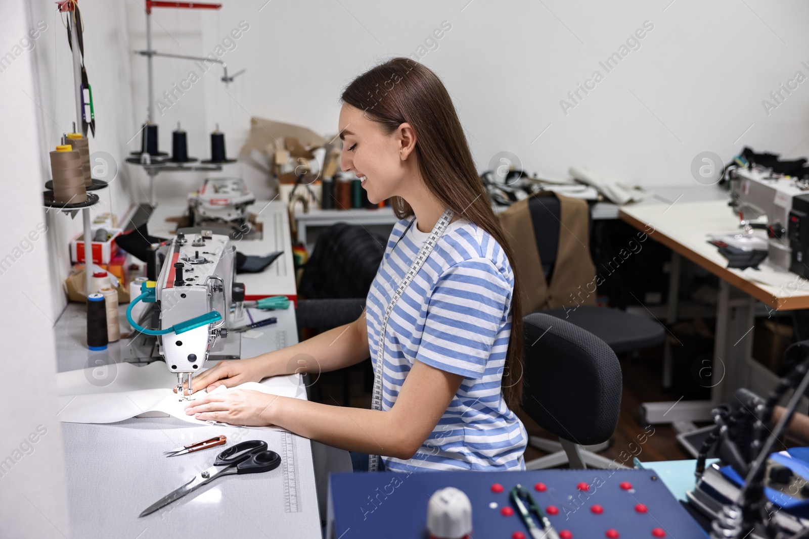 Photo of Young woman working with sewing machine in professional workshop