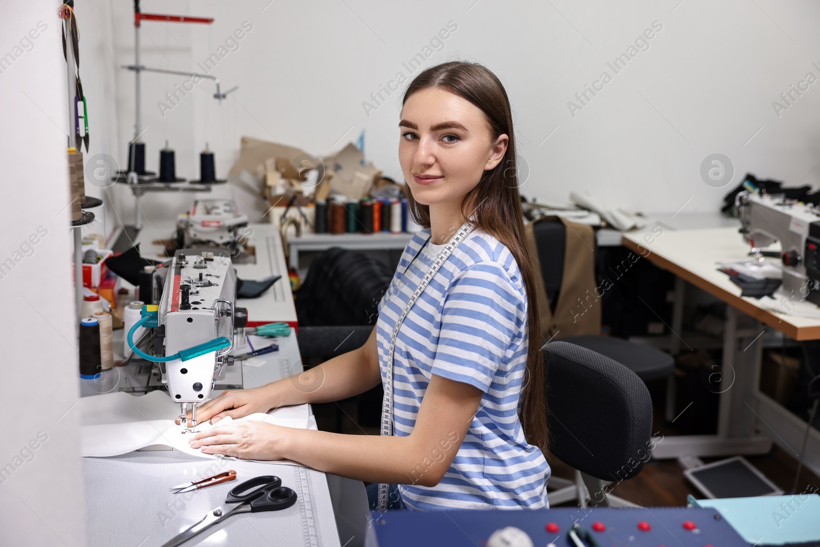 Photo of Young woman working with sewing machine in professional workshop