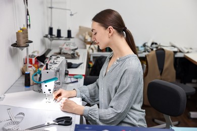 Photo of Young woman working with sewing machine in professional workshop