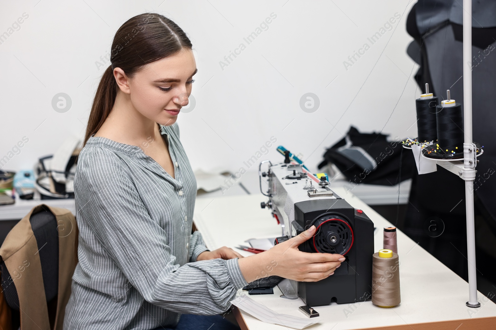 Photo of Young woman working with sewing machine in professional workshop