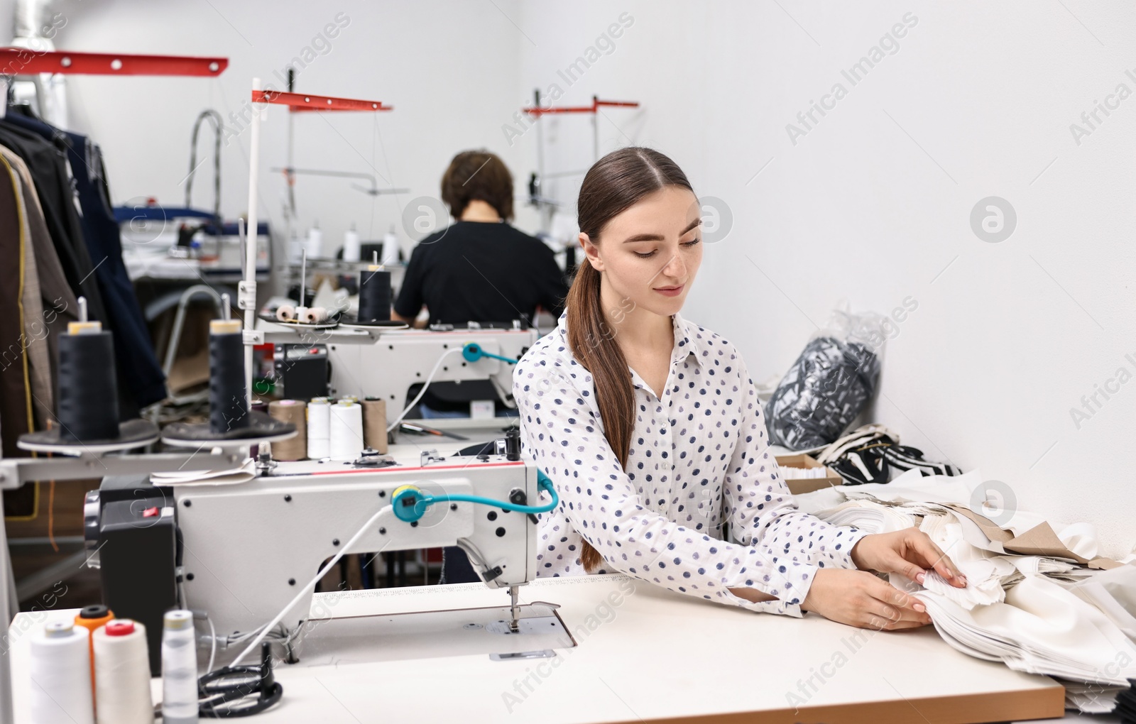 Photo of Young woman with sewing machine working at white table in professional workshop