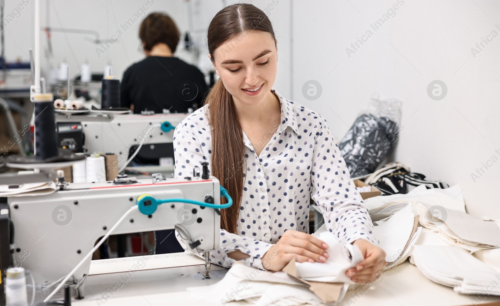 Photo of Young woman with sewing machine working at white table in professional workshop