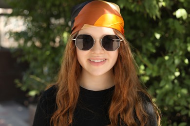 Photo of Portrait of happy teenage girl with long hair wearing sunglasses and bandana outdoors