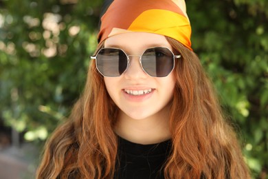 Photo of Portrait of happy teenage girl with long hair wearing sunglasses and bandana outdoors