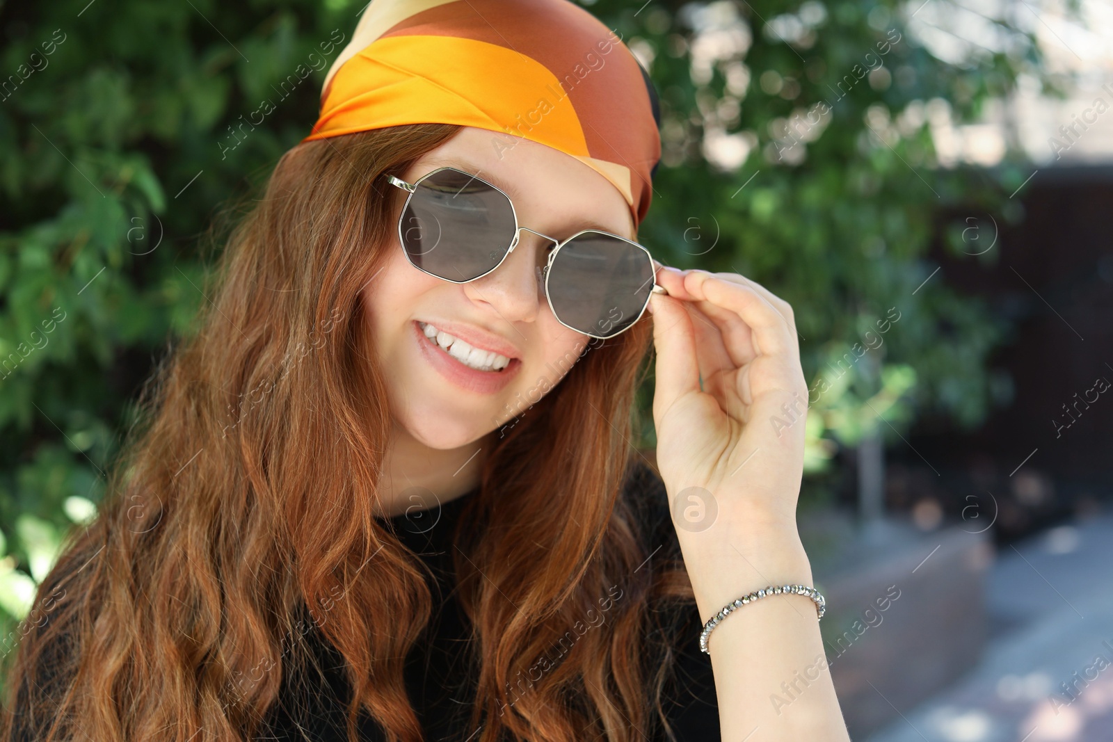 Photo of Portrait of happy teenage girl with long hair wearing sunglasses and bandana outdoors