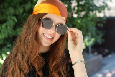 Photo of Portrait of happy teenage girl with long hair wearing sunglasses and bandana outdoors