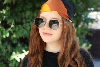 Photo of Portrait of happy teenage girl with long hair wearing sunglasses and bandana outdoors