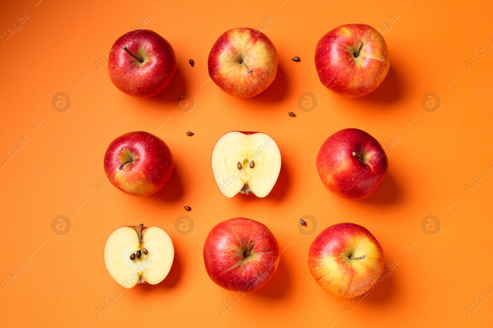 Photo of Fresh red apples and seeds on orange background, flat lay