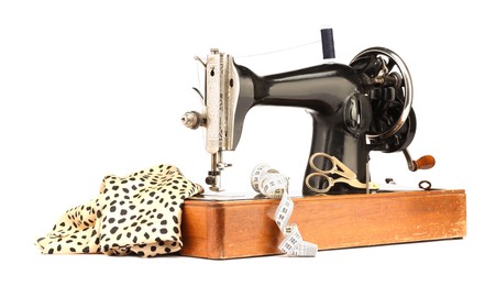 Photo of Sewing machine with fabric, measuring tape, scissors and spool of thread isolated on white