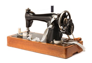 Photo of Sewing machine, measuring tape and spools of threads isolated on white