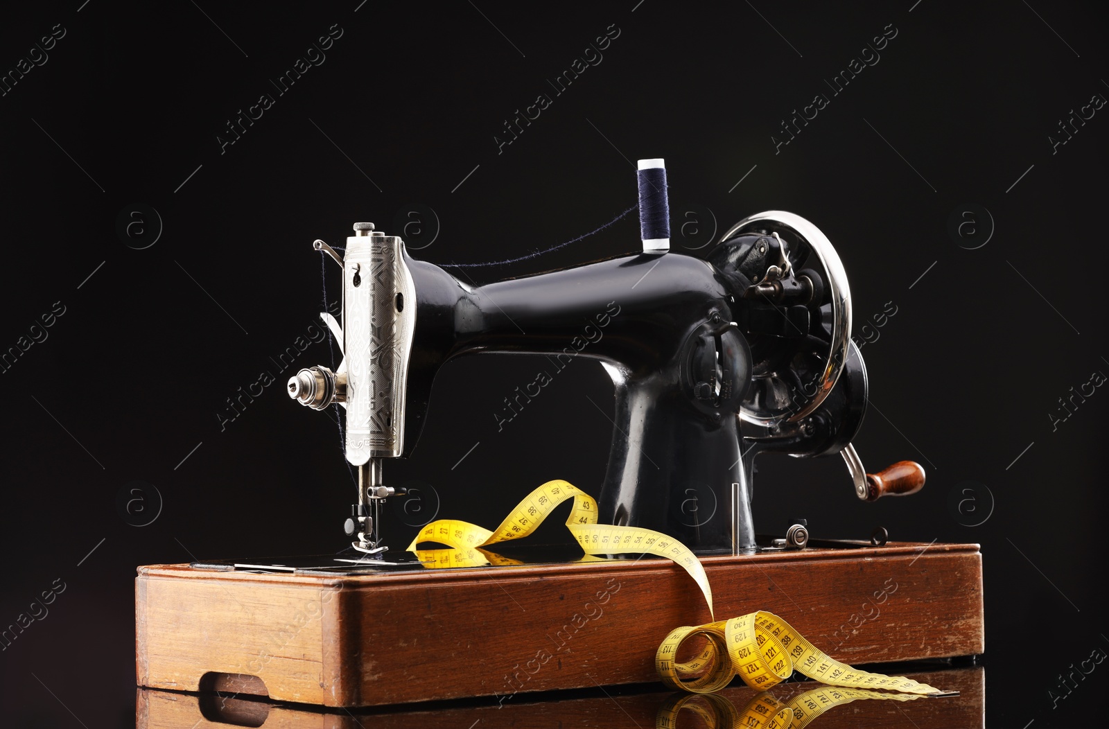 Photo of Professional sewing machine and measuring tape on black background