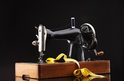 Photo of Professional sewing machine and measuring tape on black background