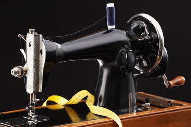 Photo of Professional sewing machine and measuring tape on black background, closeup