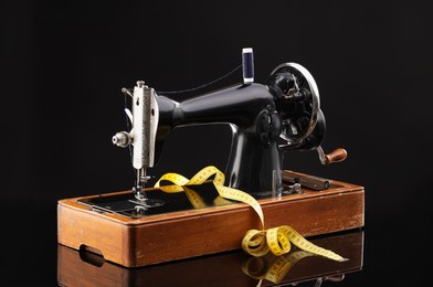 Photo of Professional sewing machine and measuring tape on black background