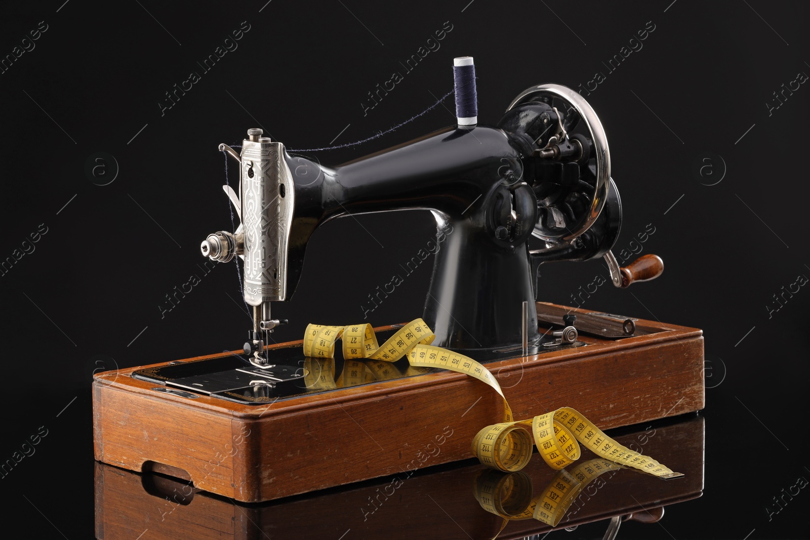 Photo of Professional sewing machine and measuring tape on black background