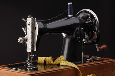 Photo of Professional sewing machine and measuring tape on black background, closeup