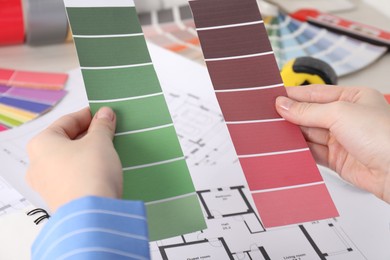 Photo of Designer with color selection chart working on house project at table, closeup