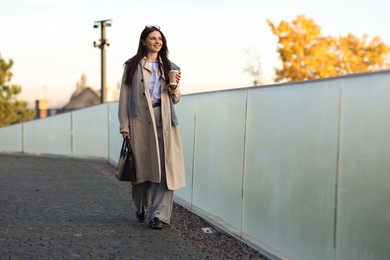 Photo of Smiling businesswoman in stylish suit with paper cup walking outdoors. Space for text