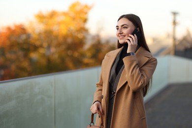 Photo of Beautiful woman in stylish suit talking on smartphone outdoors. Space for text