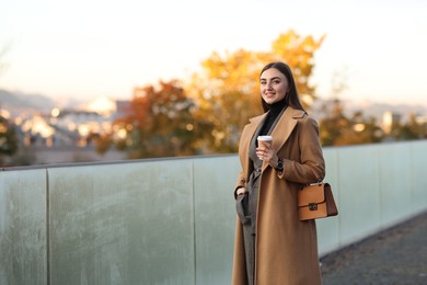 Beautiful woman in stylish suit with paper cup outdoors. Space for text