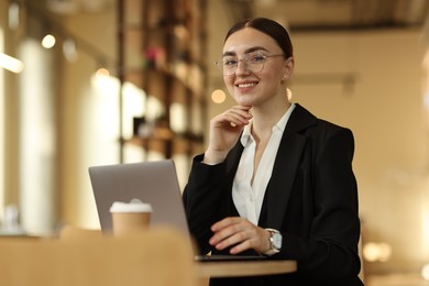 Woman in stylish formal suit working on laptop at table indoors