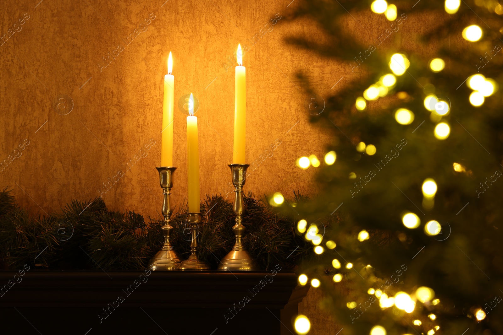 Photo of Christmas tree decorated with festive lights, burning candles and garland indoors, selective focus