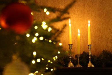 Photo of Christmas tree decorated with baubles, festive lights, burning candles and garland indoors, selective focus