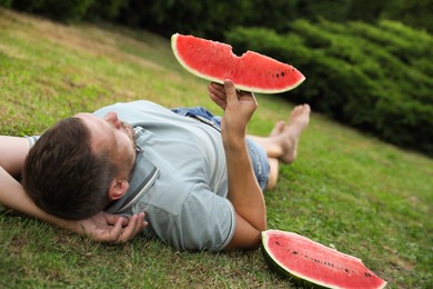 Photo of Happy man with slice of juicy watermelon on green grass outdoors