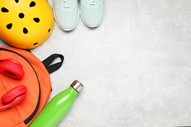 Photo of Bicycle helmet, backpack, thermo bottle and sneakers on grey textured background, flat lay. Space for text