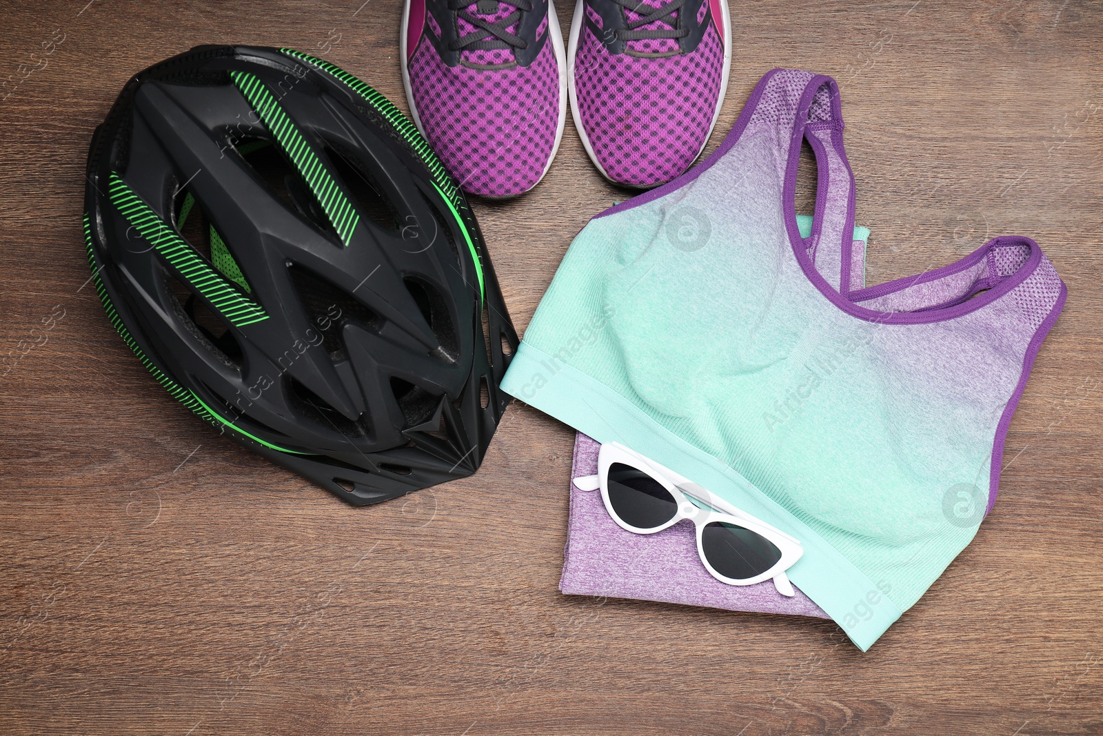 Photo of Bicycle helmet, sneakers, sunglasses and sportswear on wooden background, flat lay