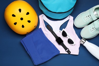 Photo of Bicycle helmet, sneakers, sportswear and accessories on blue wooden background, flat lay