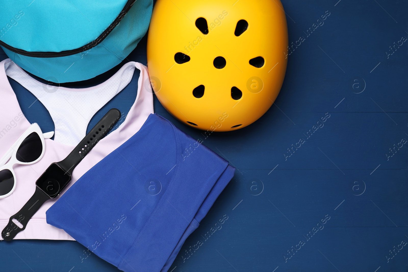 Photo of Bicycle helmet, sportswear and accessories on blue wooden background, flat lay. Space for text