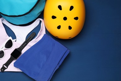 Photo of Bicycle helmet, sportswear and accessories on blue wooden background, flat lay. Space for text